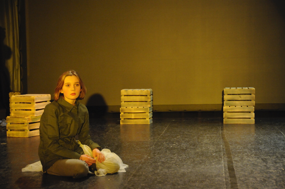 Mädchen sitzt verloren auf einer Bühne, blickt ins Leere